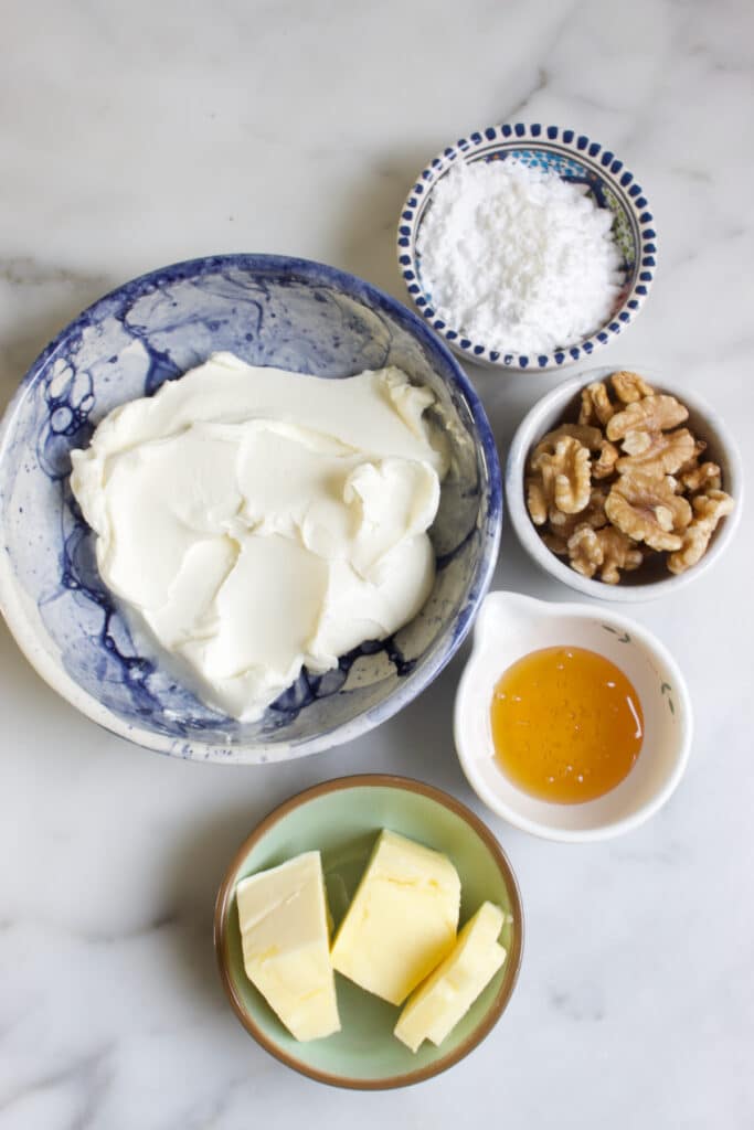 kommetjes met ingrediënten voor de roomkaas glazuur: roomkaas, poedersuiker, honing, boter en walnoten