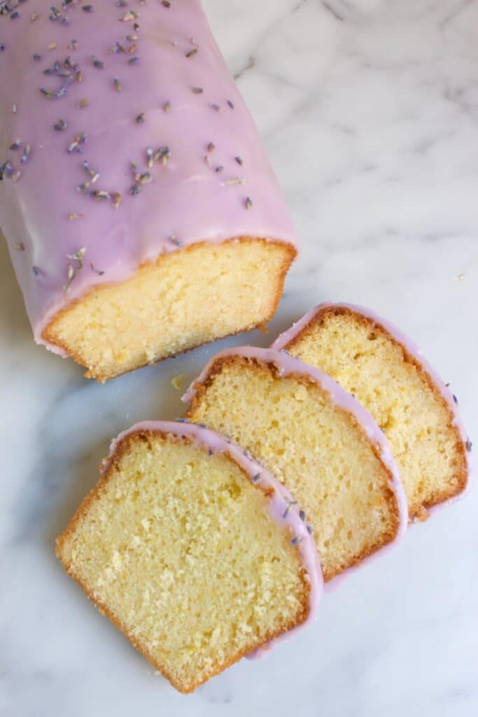 citroencake met lavendel glazuur en losse lavendbloemen erop. ervoor liggen dakpansgewijs drie stukjes van cake