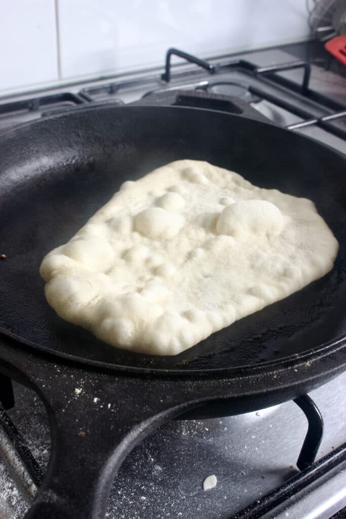 naan brood wat gebakken wordt in een gietijzeren pan